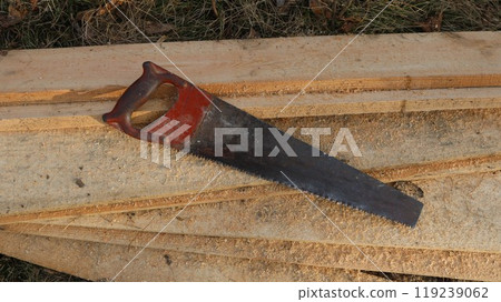 an old hacksaw lies on sawn boards strewn with sawdust like a village scene, a peasant's working hand tool at a construction site and in farm activities an old hacksaw lies on sawn boards strewn with sawdust like a village scene, a peasant's working hand tool at a construction site and in farm activities 119239062
