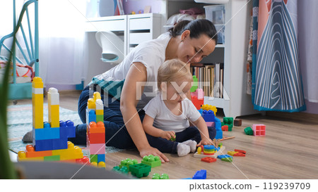 Cheerful mother and her baby share joyful moments while exploring colorful wooden toys in their nursery 119239709
