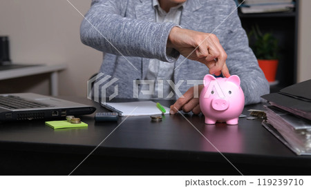 Man sits at his office desk, counting coins and placing them into a piggy bank, organizing his finances 119239710