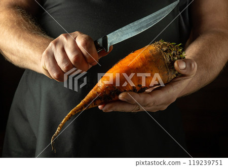 A cook cuts beets to add to food or borscht. Close-up of the chef hands holding an orange beet and a knife A cook cuts beets to add to food or borscht. Close-up of the chef hands holding an orange beet and a knife 119239751