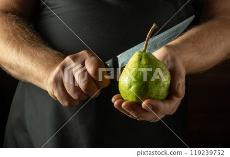A chef tries to cut a green pear with a knife. Low key concept of making pear dessert in the kitchen 119239752