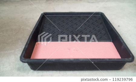 Black paint tray holding pink paint on concrete floor. 119239796