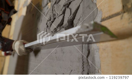 Construction worker checking level of plaster on wall with spirit level. 119239797