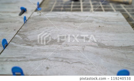 Worker installing large ceramic tiles with leveling system. 119240538