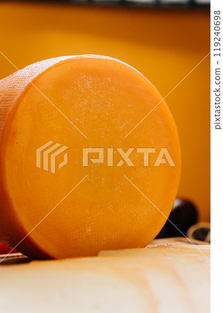 Round cheese wheel on a wooden board with fresh vegetables and spices in a rustic kitchen setup Round cheese wheel on a wooden board with fresh vegetables and spices in a rustic kitchen setup 119240698