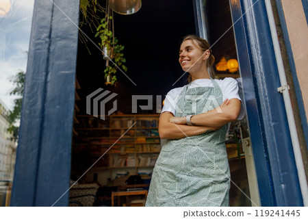 A Cheerful Smiling Barista Welcoming Customers at the Entrance of a Cafe on a Beautiful Sunny Day A Cheerful Smiling Barista Welcoming Customers at the Entrance of a Cafe on a Beautiful Sunny Day 119241445