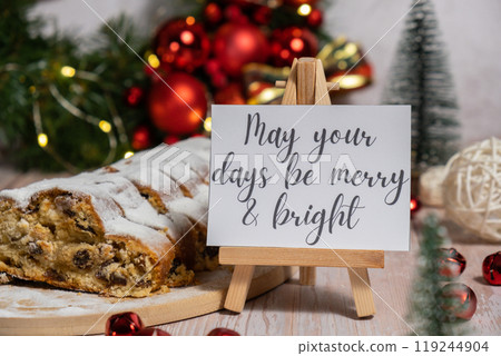 Paper note with text MAY YOUR DAYS BE MERRY AND BRIGHT congratulations. Homemade Christmas traditional cake pie with marzipan nuts and dried fruits pastry dessert stollen. Winter holidays season 119244904