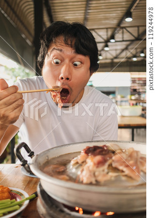 Happy and excited face man eating Moo Kra Ta or Thai BBQ buffet. 119244978