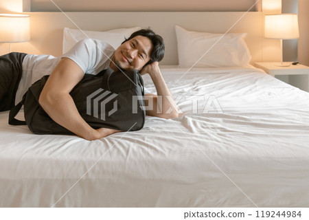 Happy man lying on the hotel bed with luggage travel bag. 119244984