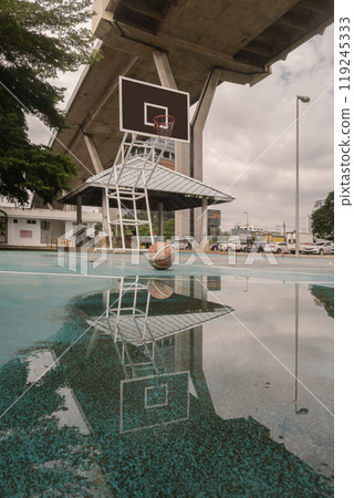 Basketball ball on the Old cement court floor with the reflection of them on puddle of rainwater. Basketball ball on the Old cement court floor with the reflection of them on puddle of rainwater. 119245333
