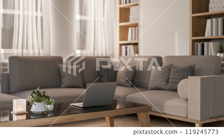 A laptop on a coffee table beside a large grey corner sofa in a contemporary living room. 119245773
