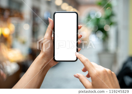 A woman's hand holding a smartphone, set against a blurred background of a market or mall. 119245829