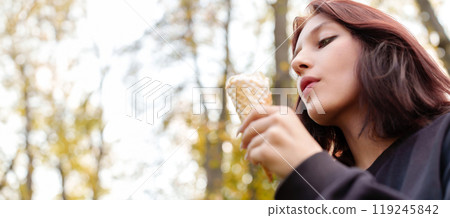 Teenage girl with striking looks playfully savors creamy ice cream cone in autumn park, tongue piercing adding hint of intrigue Teenage girl with striking looks playfully savors creamy ice cream cone in autumn park, tongue piercing adding hint of intrigue 119245842