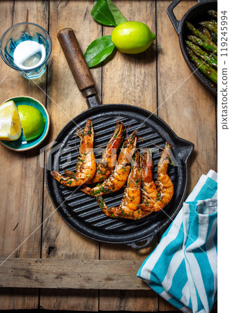 Grilled shrimp on a black grill pan on a rustic wooden table, with limes, a blue-striped cloth Grilled shrimp on a black grill pan on a rustic wooden table, with limes, a blue-striped cloth 119245994
