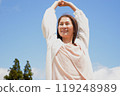 A smiling woman raising her arms in the air under the blue sky 119248989