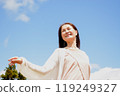 A smiling senior woman relaxing with her arms outstretched under the blue sky 119249327