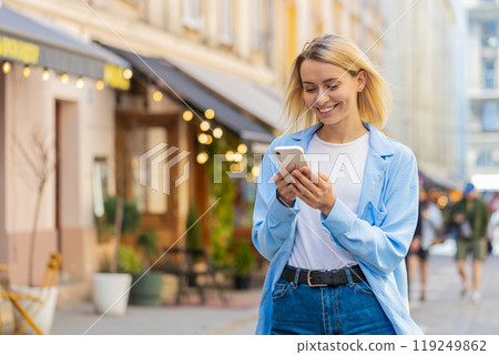 Happy woman using smartphone typing texting social media application messages e-mail on city street Happy woman using smartphone typing texting social media application messages e-mail on city street 119249862