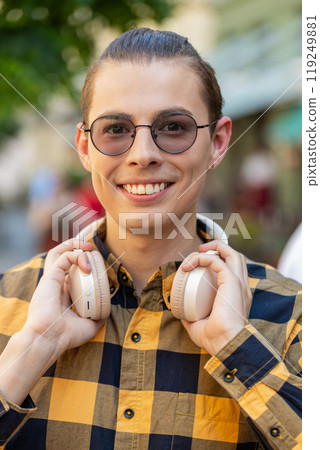 Happy smiling man listening music taking off wireless headphones looking at camera on city street 119249881