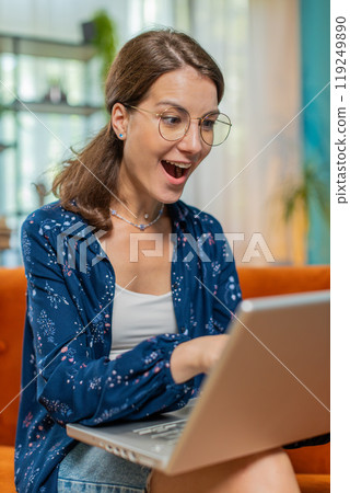 Surprised happy young woman in eyeglasses using laptop computer, receive good news message at home Surprised happy young woman in eyeglasses using laptop computer, receive good news message at home 119249890