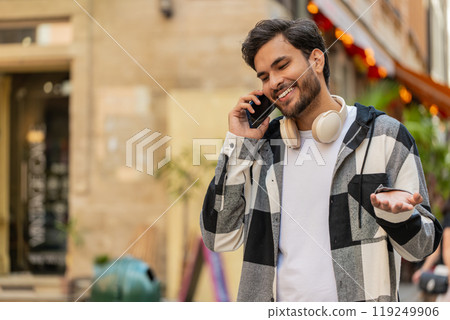 Indian young man tourist on smartphone, chatting with friend while walking in the city street Indian young man tourist on smartphone, chatting with friend while walking in the city street 119249906
