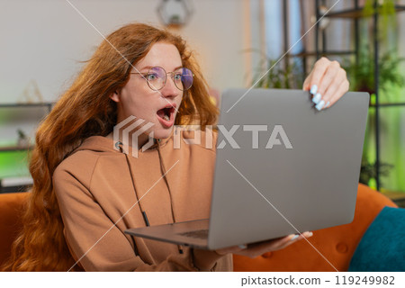 Surprised Caucasian redhead woman with windswept hair using laptop sitting on couch at home Surprised Caucasian redhead woman with windswept hair using laptop sitting on couch at home 119249982