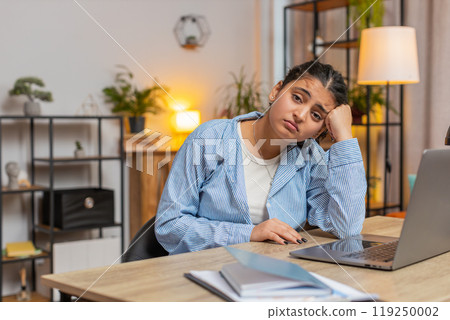 Sad Indian young woman freelancer looks pensive thinks over life concerns sitting at desk at home Sad Indian young woman freelancer looks pensive thinks over life concerns sitting at desk at home 119250002