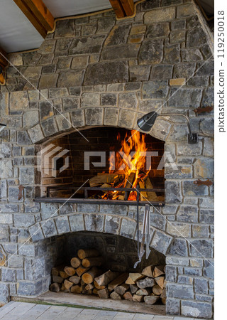 Burning stone barbecue firewood with fire, open brick oven for cooking food meat fish in backyard 119250018