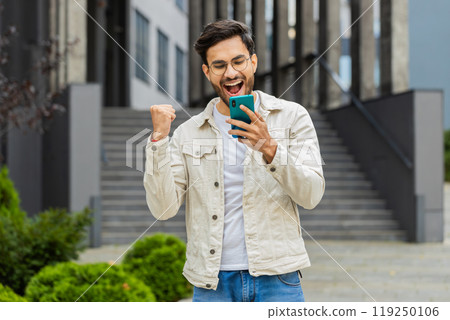 Indian man use mobile smartphone celebrating win good message news outdoors in urban city street 119250106