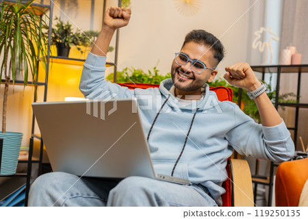 Amazed Indian man use laptop computer, receive good news message shocked by victory, celebrate win 119250135