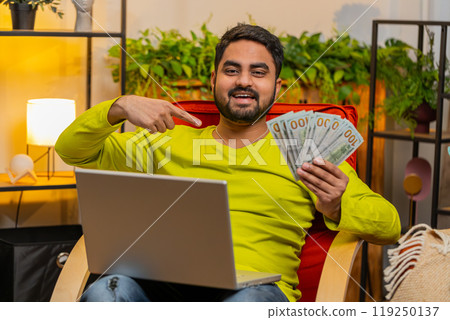 Smiling happy man counting money cash and use laptop pc calculate domestic income earnings at home Smiling happy man counting money cash and use laptop pc calculate domestic income earnings at home 119250137