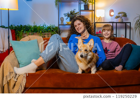 Happy family mother and daughter sitting beside corgi dog watching TV in living room at home Happy family mother and daughter sitting beside corgi dog watching TV in living room at home 119250229