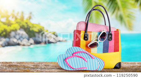A beach bag with towels, sunglasses, and flip flops placed on a table A beach bag with towels, sunglasses, and flip flops placed on a table 119250590