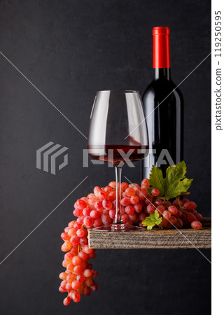 A glass and bottle of wine paired with grapes, set against a dark background 119250595