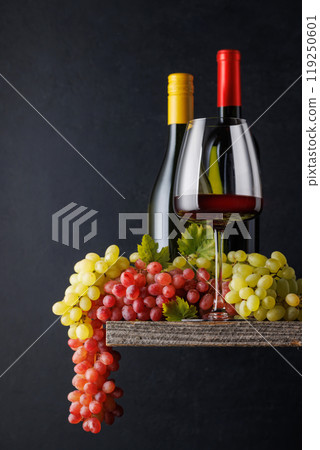 A glass and bottles of wine paired with grapes, set against a dark background 119250601