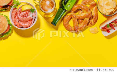 A vibrant photo showcasing a glass of beer surrounded by various snacks and fast food 119250709
