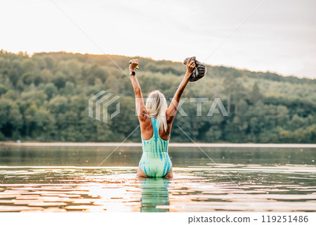 Cold water swimming for elderly woman. Rear view of senior sporty woman standing in lake during cold morning. Cold water swimming for elderly woman. Rear view of senior sporty woman standing in lake during cold morning. 119251486