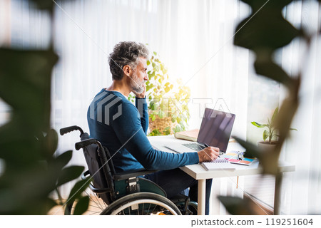 Handsome man in wheelchair working from home office, making phone call and writing notes in planner. Telecommuting and home office. Handsome man in wheelchair working from home office, making phone call and writing notes in planner. Telecommuting and home office. 119251604