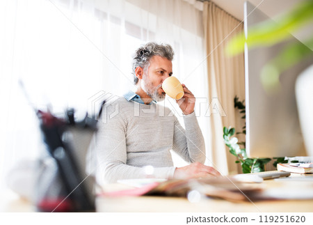 Homeoffice for handsome man. Man drinking coffee in the morning, working on computer from home. Telecommuting. Homeoffice for handsome man. Man drinking coffee in the morning, working on computer from home. Telecommuting. 119251620