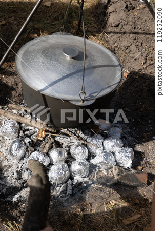 Potatoes wrapped in foil are baked in coals. Camping pot with lid. Cooking food on a campfire on a hike. Fire coals. Potatoes wrapped in foil are baked in coals. Camping pot with lid. Cooking food on a campfire on a hike. Fire coals. 119252090