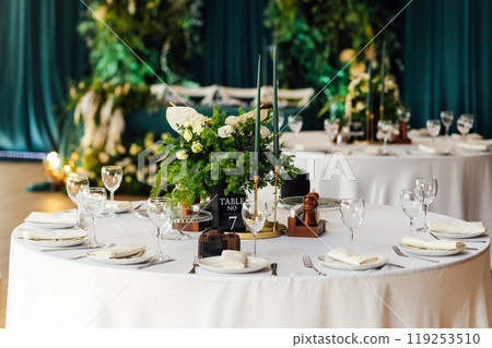 Luxurious restaurant. Luxurious interior, white tables, serving dishes and glasses for guests. Green decor Luxurious restaurant. Luxurious interior, white tables, serving dishes and glasses for guests. Green decor 119253510
