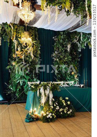 Luxurious restaurant. Luxurious interior, white tables, serving dishes and glasses for newlyweds. Green decor 119253517