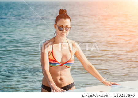 Sea woman sup. Silhouette of happy middle aged tanned woman in rainbow bikini, surfing on SUP board, confident paddling through water surface. Idyllic sunset. Active lifestyle at sea or river. 119253670