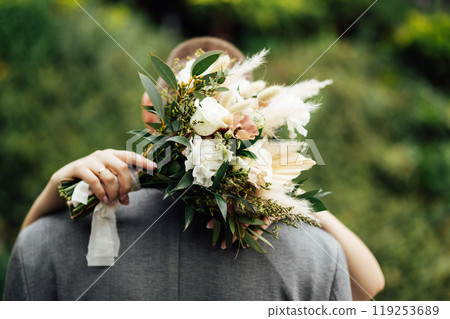 The bride and groom are hugging. The bride hugs the groom's neck and holds her bouquet of flowers 119253689