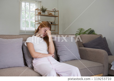 Young Woman Sitting on Sofa with Headache, Holding Head in Pain, Stress and Fatigue Concept 119253710
