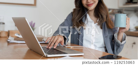 Young Female Freelancer Working Online from Home with Laptop and Coffee in Modern Home Office Setting 119253863