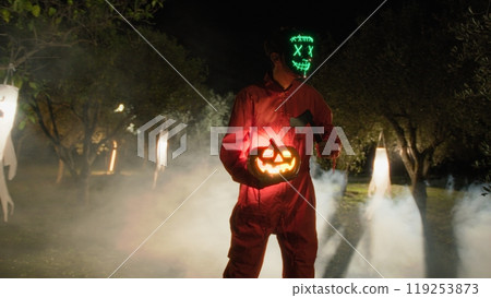 Anonymous Man in Glowing Mask with Halloween Pumpkin And Axe Anonymous Man in Glowing Mask with Halloween Pumpkin And Axe 119253873