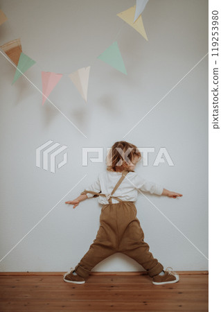Portrait of an adorable little girl standing under paper garland. 119253980