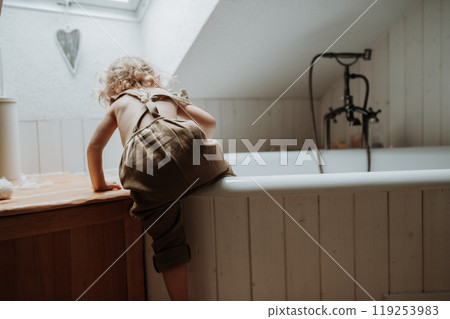 Little girl is climbing into an empty bathtub in the bathroom. Little girl is climbing into an empty bathtub in the bathroom. 119253983