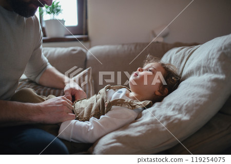 Father taking care of sick girl with fever and cold at home. Daughter lying on sofa, feeling tired. Father taking care of sick girl with fever and cold at home. Daughter lying on sofa, feeling tired. 119254075
