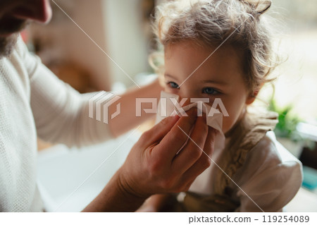 Sick girl with cold at home. Father helping little daughter to blow her nose. 119254089